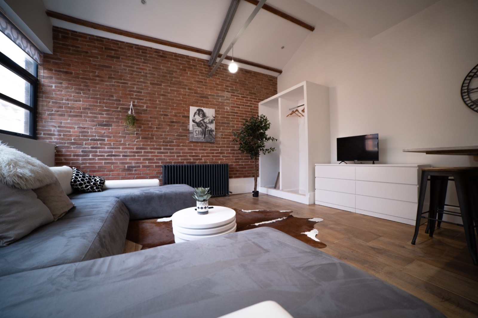 Open-plan studio with exposed brick, corner sofa and open wardrobe